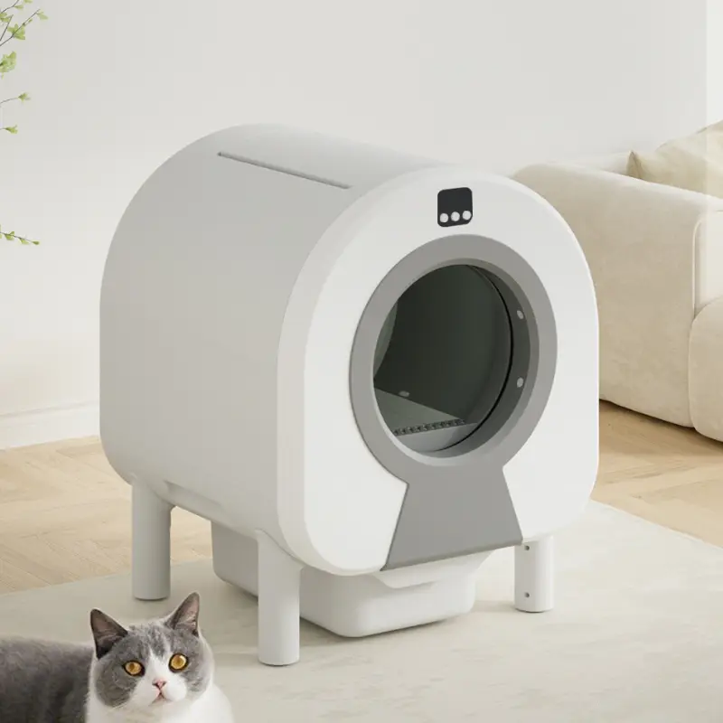 White enclosed smart cat litter box in a modern living room with a gray cat nearby.